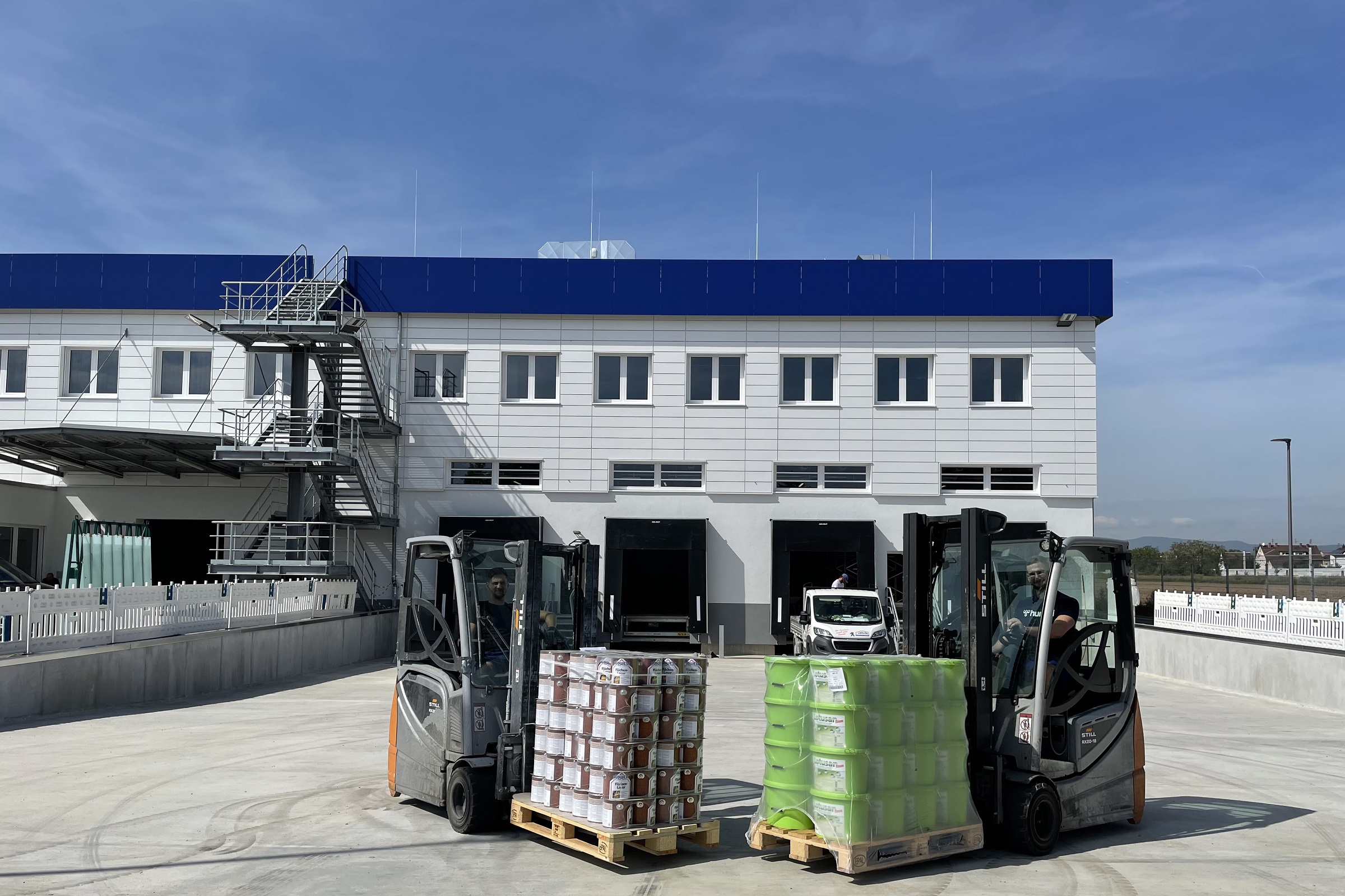 Two forklifts with color pallets in front of the new logistics center.